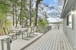 A wooden deck with a table and chairs, surrounded by trees. - Lake-view Cabin w/ Furnished Deck in Hadley! (Hadley)