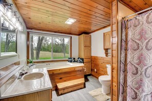 Baño de cabaña de madera con una ventana grande, una bañera de madera, un lavamanos y un inodoro.