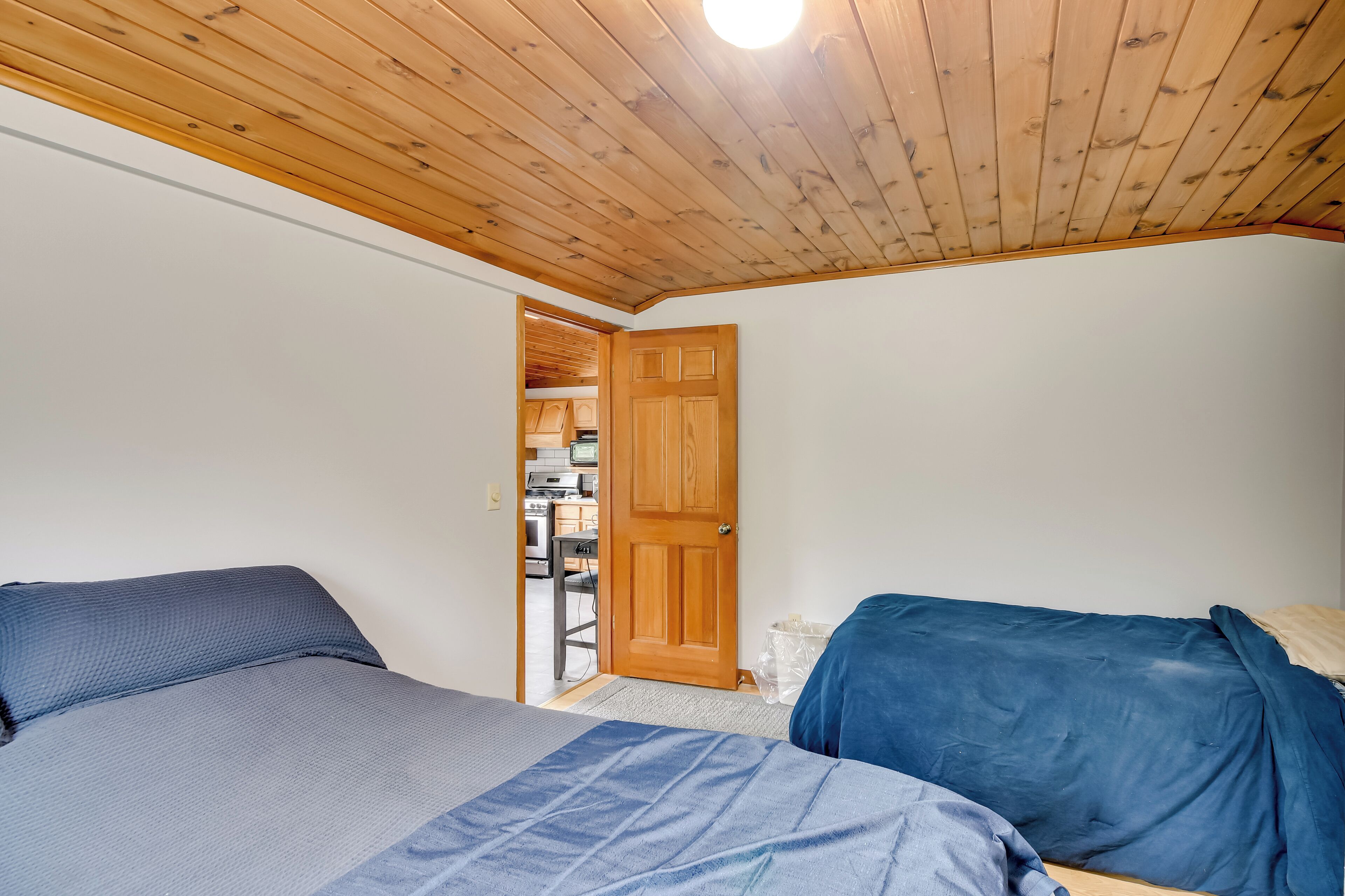 A bedroom with two beds, wooden ceiling, and a door leading to a kitchen area.