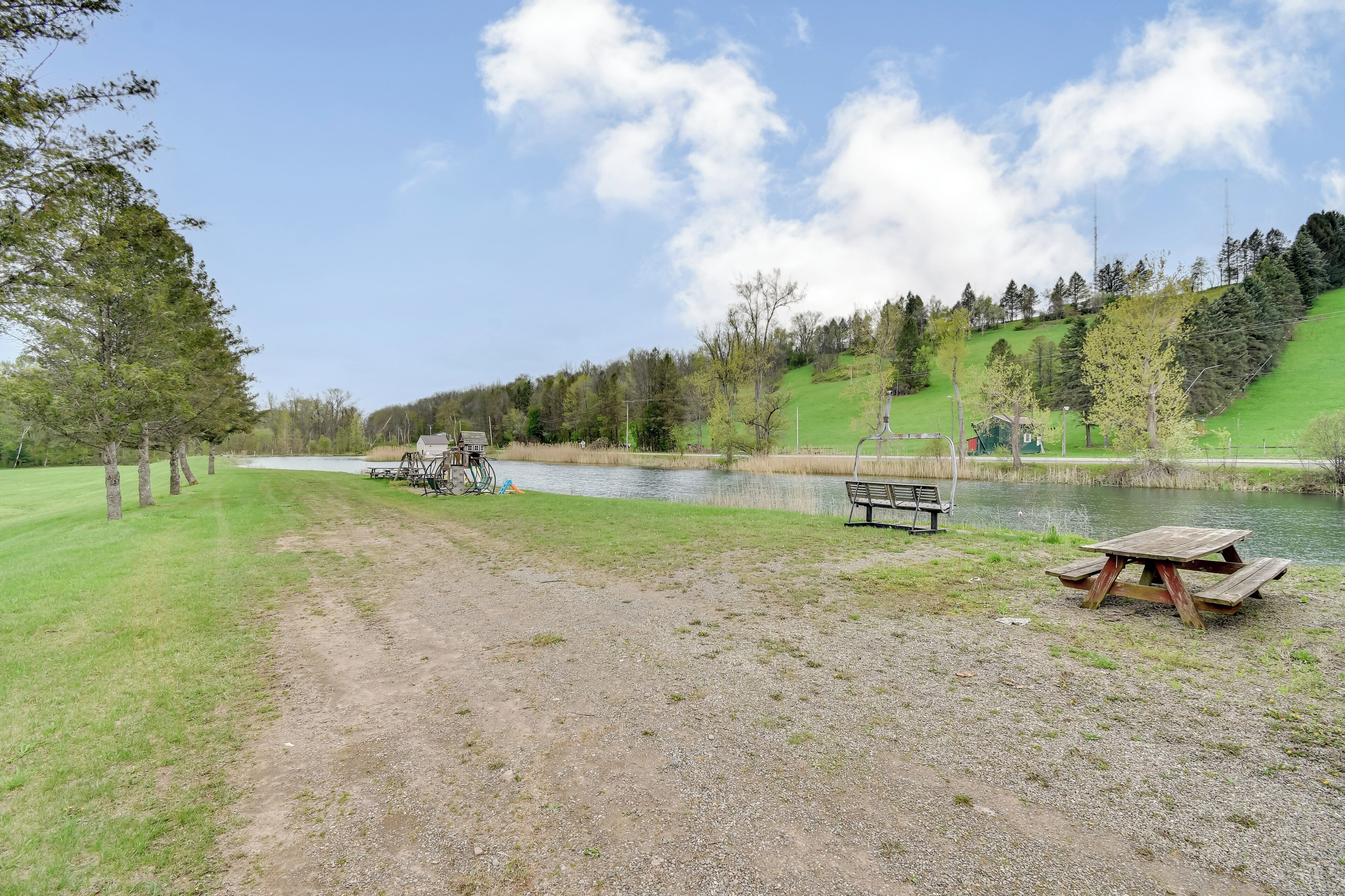 A picnic table and bench by a lake with a dirt path leading to it.