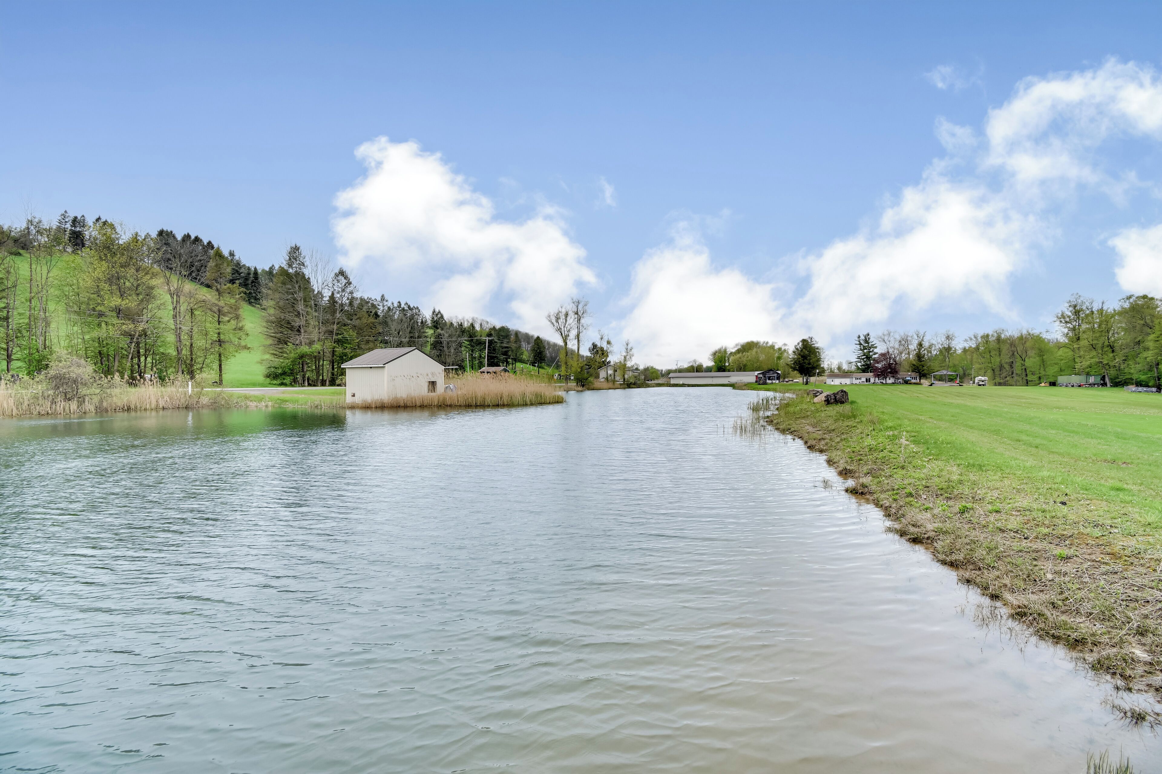 A river with a small building on the left bank, a grassy area, and trees in the background.