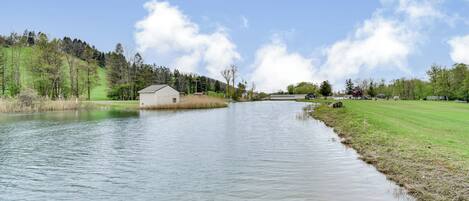 A river with a small building on the left bank, a grassy area, and trees in the background.