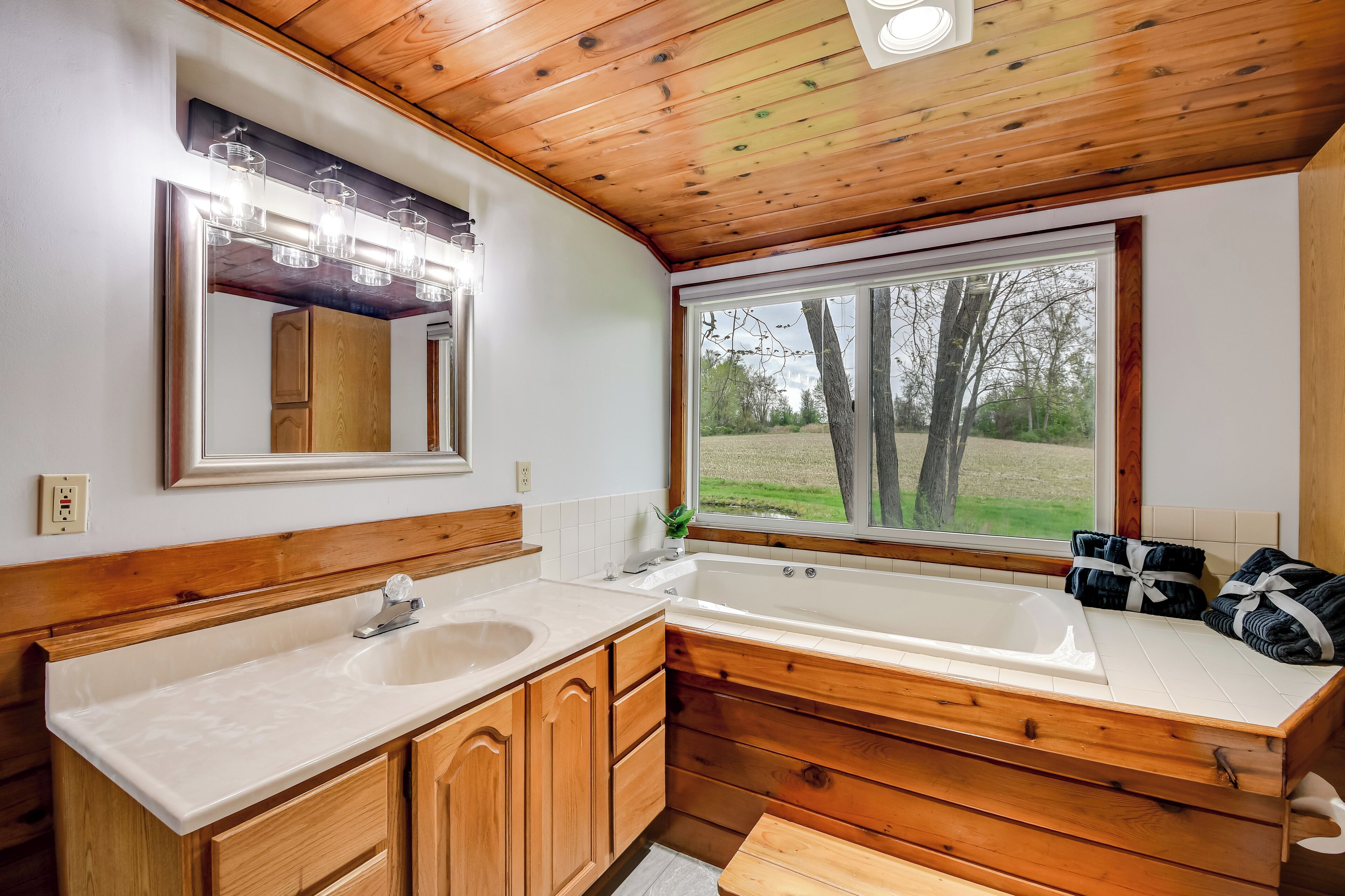 A bathroom with wooden cabinetry, a double sink, and a large window with a view of trees.