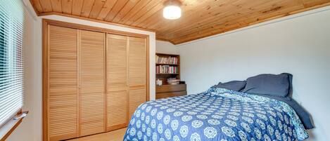 Un dormitorio con techo de madera, una cama grande con edredón azul y blanco estampado, una estantería y un armario de madera.