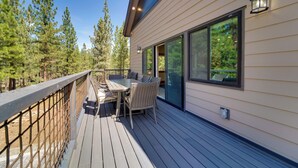Eine Terrasse mit Gartenmöbeln, einem Geländer und einem großen Fenster mit Blick auf einen Wald.