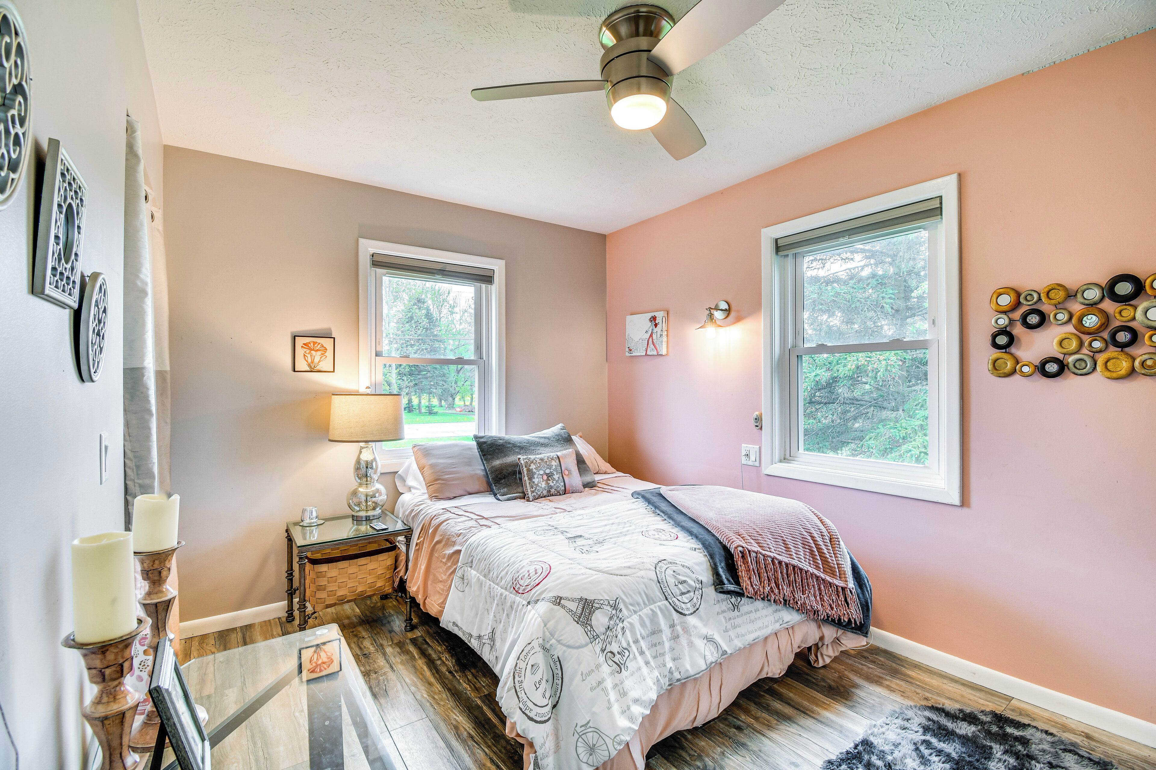 A bedroom with a bed, bedside tables, a lamp, a ceiling fan, and a wall with decorative plates.