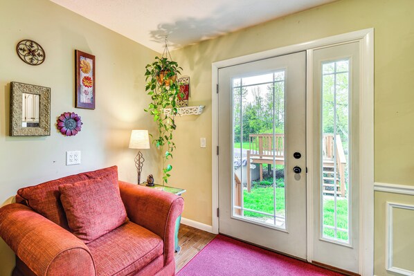 A living room with a red sofa, a hanging plant, and a door leading to a backyard.