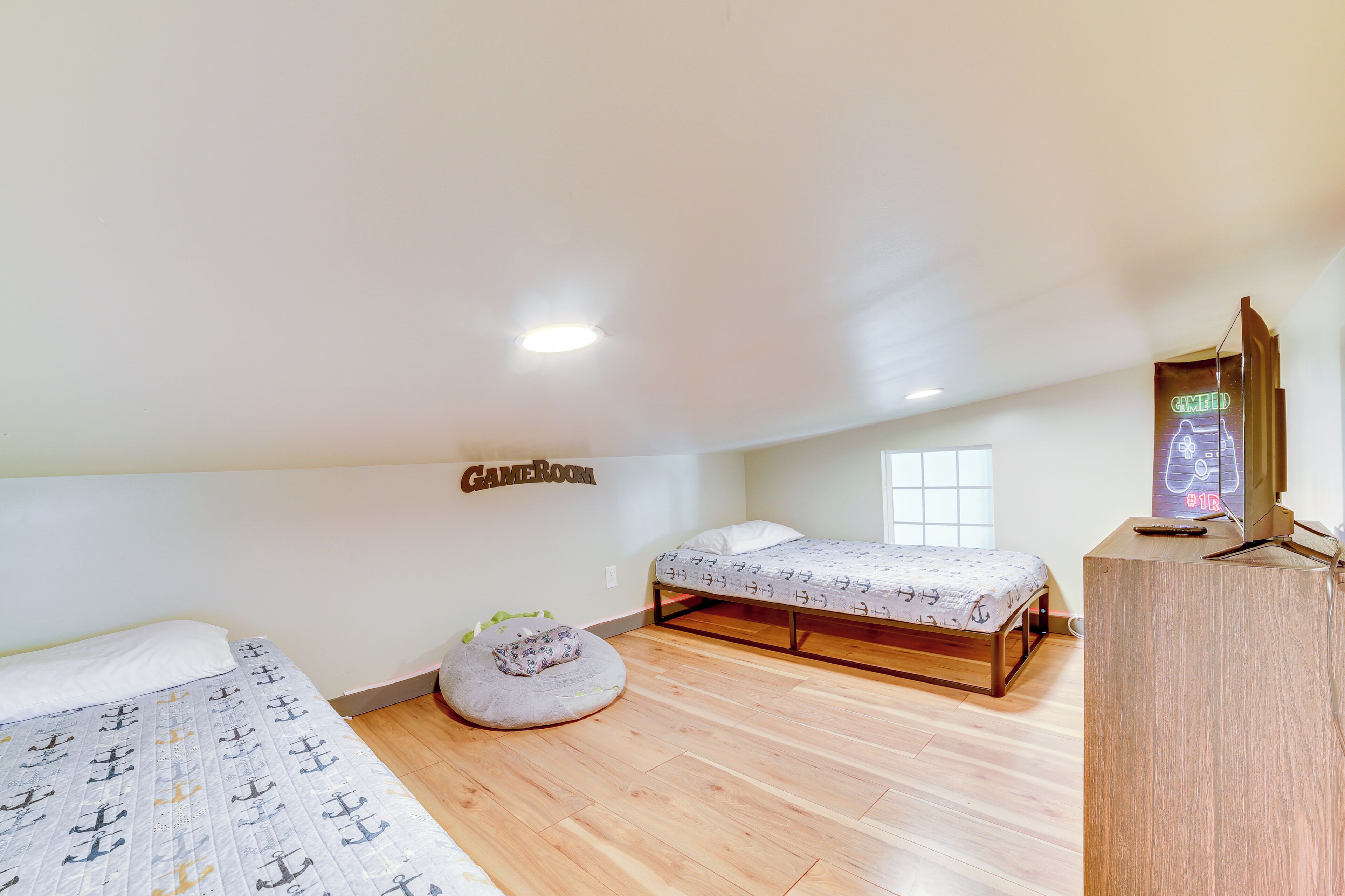 Un dormitorio con dos camas, un sillón de peluche, un televisor y un letrero de neón en la pared.