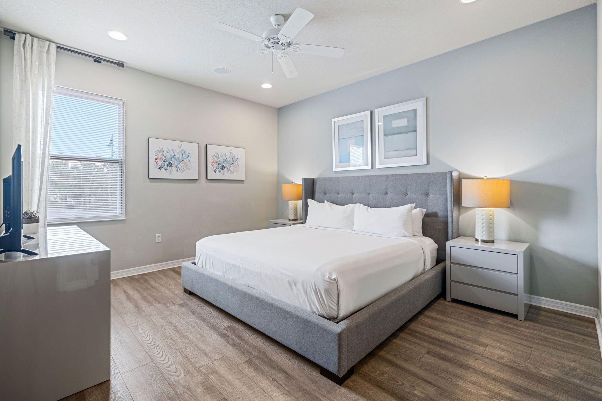 Quarto com uma cama grande, duas mesas de cabeceira com luminárias, um ventilador de teto e obras de arte nas paredes.