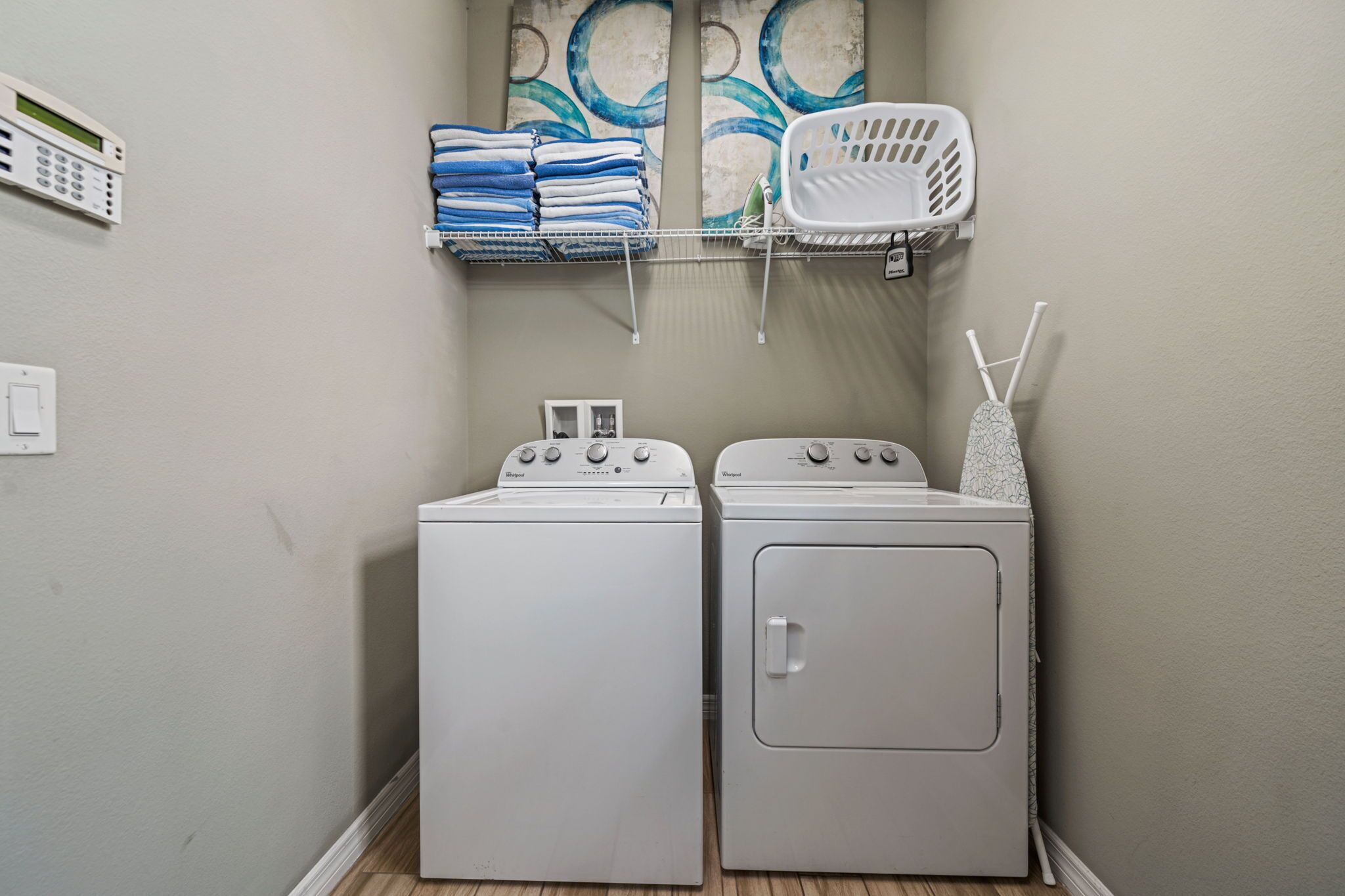 A laundry area with two white washing machines, a shelf with folded towels, and a white laundry basket.