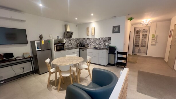 Une cuisine moderne avec un coin repas comprenant une table ronde et des chaises, un four encastré et un téléviseur fixé au mur.
