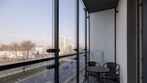 A balcony with a view of a road and buildings. There are two chairs and a table on the balcony.