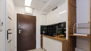 A compact kitchen with white cabinets, a wooden countertop, a microwave, and a small refrigerator.