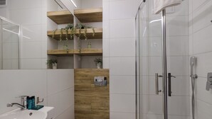 A modern bathroom with a glass shower enclosure, a white toilet, and wooden shelves with plants.