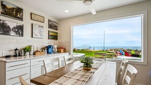 A kitchen with white cabinets, a wooden dining table, and a large window overlooking a beach. - Lakefront Cabin Hot Tub, Dock, and Adventure Shed (Sturgeon Bay)