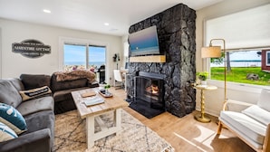 A modern living room with a stone fireplace, a large TV, and a view of the ocean. - Lakefront Cabin Hot Tub, Dock, and Adventure Shed (Sturgeon Bay)