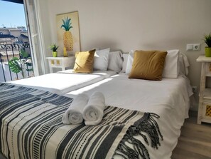 A hotel room with a bed, pillows, a blanket, a painting, and a view of buildings.