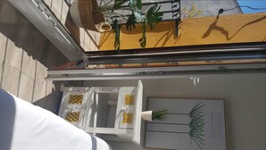 Una stanza con un letto, un tavolo bianco decorato e una pianta sospesa al muro, oltre a una stampa botanica incorniciata.