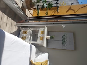 A room with a bed, a white table with decorative items, a wall-mounted plant, and a framed botanical illustration.