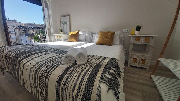 Camera da letto con un letto grande, una finestra, un comodino con una pianta e un piccolo armadietto bianco.