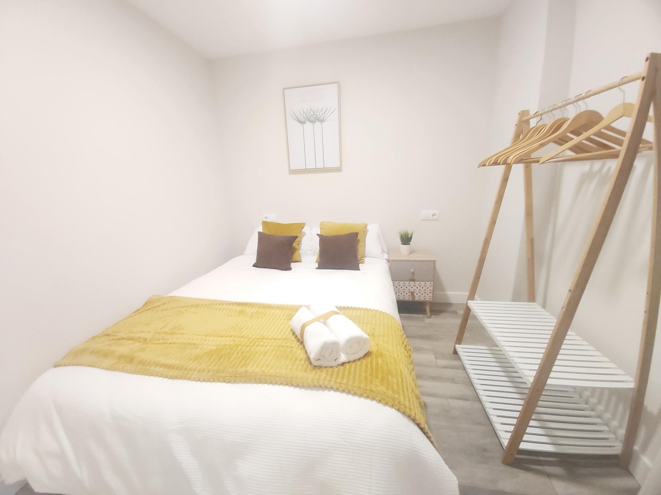 Une chambre à coucher comprenant un lit, des oreillers, une table de chevet, une œuvre d’art accrochée au mur et un porte-manteau en bois.