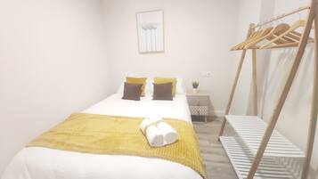 Une chambre à coucher comprenant un lit, des oreillers, une table de chevet, une œuvre d’art accrochée au mur et un porte-manteau en bois.