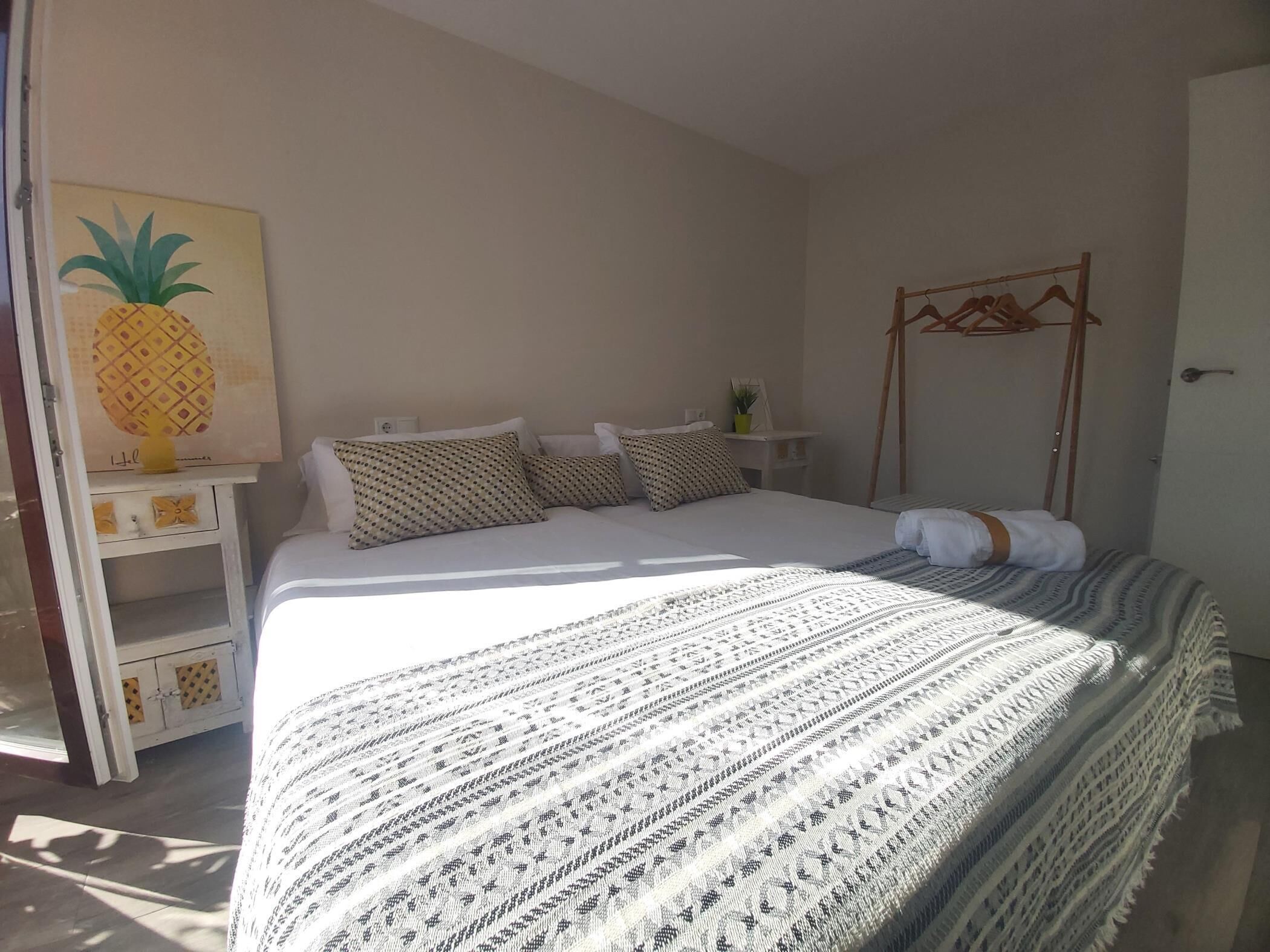 Une chambre à coucher comprenant un lit, des oreillers, une table de chevet, une plante fixée au mur et un porte-manteau en bois.