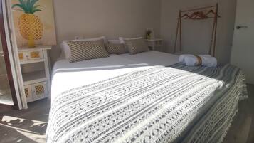 Une chambre à coucher comprenant un lit, des oreillers, une table de chevet, une plante fixée au mur et un porte-manteau en bois.