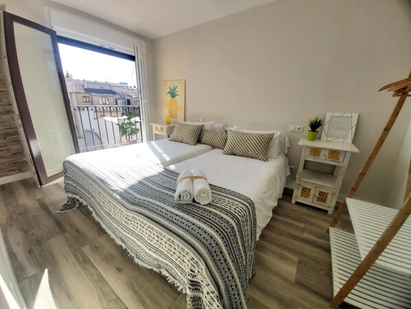 A bedroom with a large bed, a balcony, a small table with a plant, and a wall with a pineapple artwork.