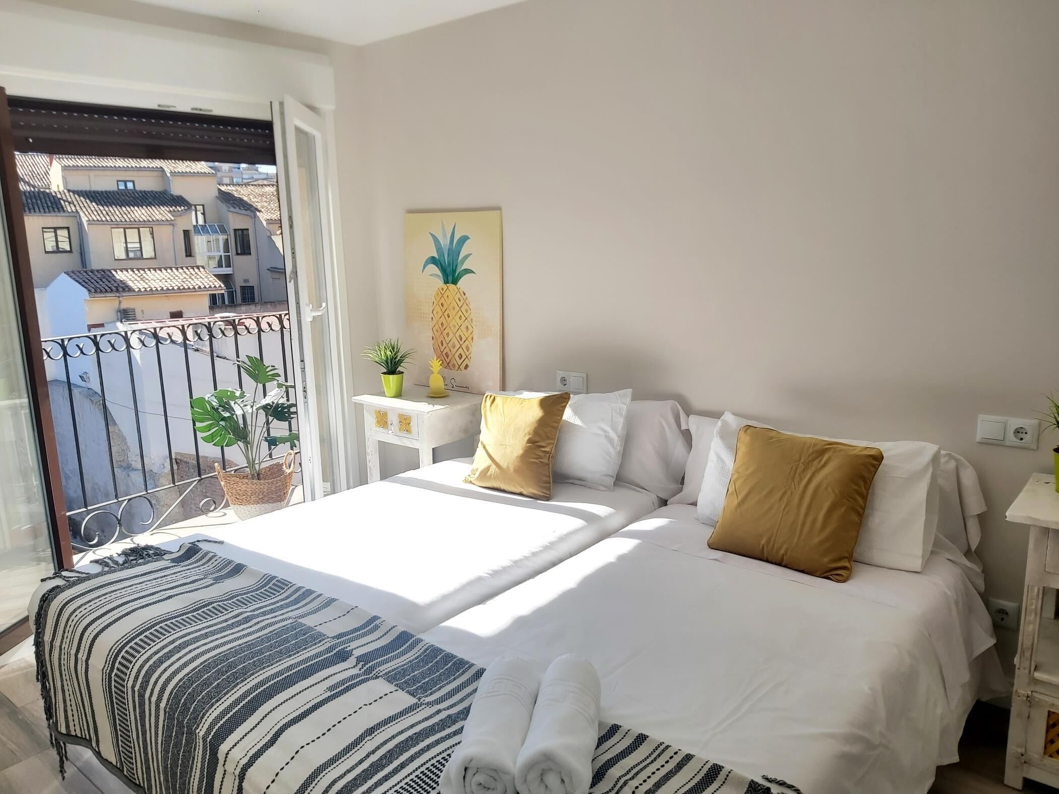 Una camera d'albergo con un letto, un comodino, una pianta in vaso e vista sui palazzi.