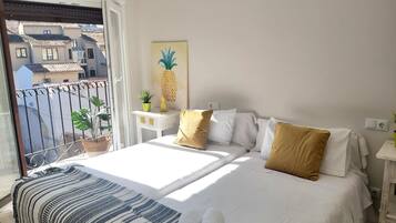Una camera d'albergo con un letto, un comodino, una pianta in vaso e vista sui palazzi.