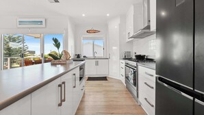 Une cuisine moderne avec des meubles blancs, un réfrigérateur en acier inoxydable et une grande fenêtre donnant sur l’extérieur.