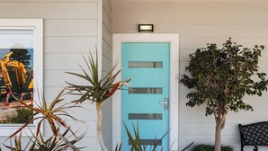 Une porte bleue avec une petite fenêtre, un arbre en pot et un banc.