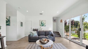 Un salon moderne avec un canapé gris, une table basse blanche et une grande fenêtre donnant sur l’extérieur.