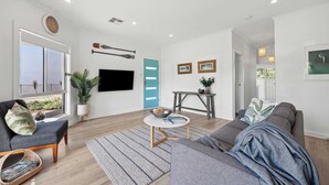 Un salon moderne avec un canapé, une table basse, un téléviseur et une fenêtre équipée de stores.