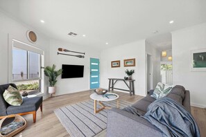 Uma sala de estar moderna com sofá, mesa de centro, TV e janela com persianas.