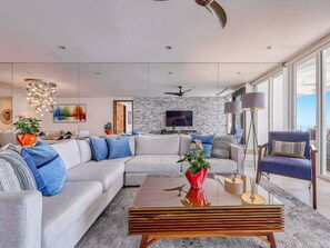 A modern living room with a sectional sofa, a coffee table, and a TV mounted on a brick wall.