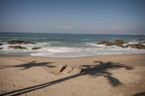 A beach with a clear sky, waves, and shadows of palm trees on the sand.