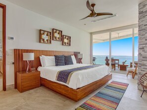 A bedroom with a large bed, wooden headboard, bedside tables, a ceiling fan, and a view of the ocean. - Oceanfront 3BR | Pools, Spa, Gym & Restaurants (Puerto Vallarta)
