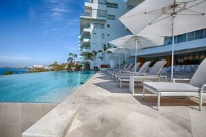 A poolside area with lounge chairs and umbrellas, a clear view of the ocean, and a modern building in the background.
