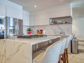 A modern kitchen with a central island, stainless steel appliances, and a marble countertop.