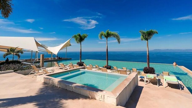 A poolside area with lounge chairs, palm trees, and a view of the ocean.