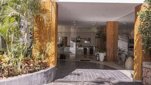 A modern hotel entrance with a glass facade, a tiled entrance area, and vertical wooden slats.