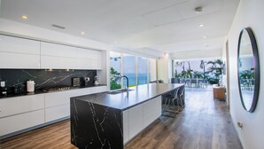 A modern kitchen with a large island, white cabinetry, and a view of the ocean.