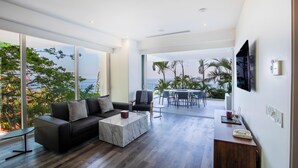 A modern living room with a sofa, coffee table, and TV. There is a dining area with chairs and a table.