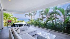 A modern living room with a large glass wall, a sofa, a coffee table, and a dining area with a table and chairs.