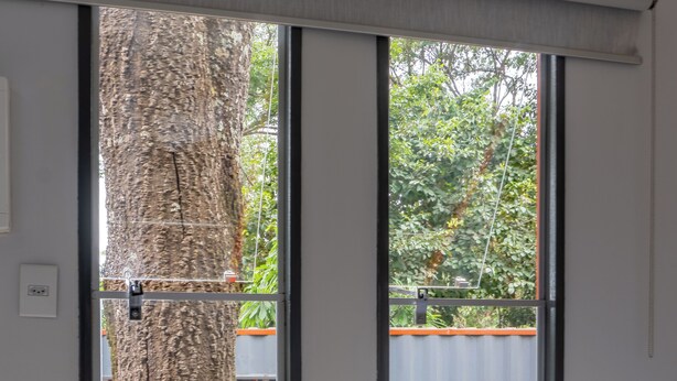 A bedroom with a large sliding glass door leading to an outdoor area, a bed with a brown blanket, and a view of a tree and a fence. - Vila Ecco Cubo (Alto Paraiso de Goias)