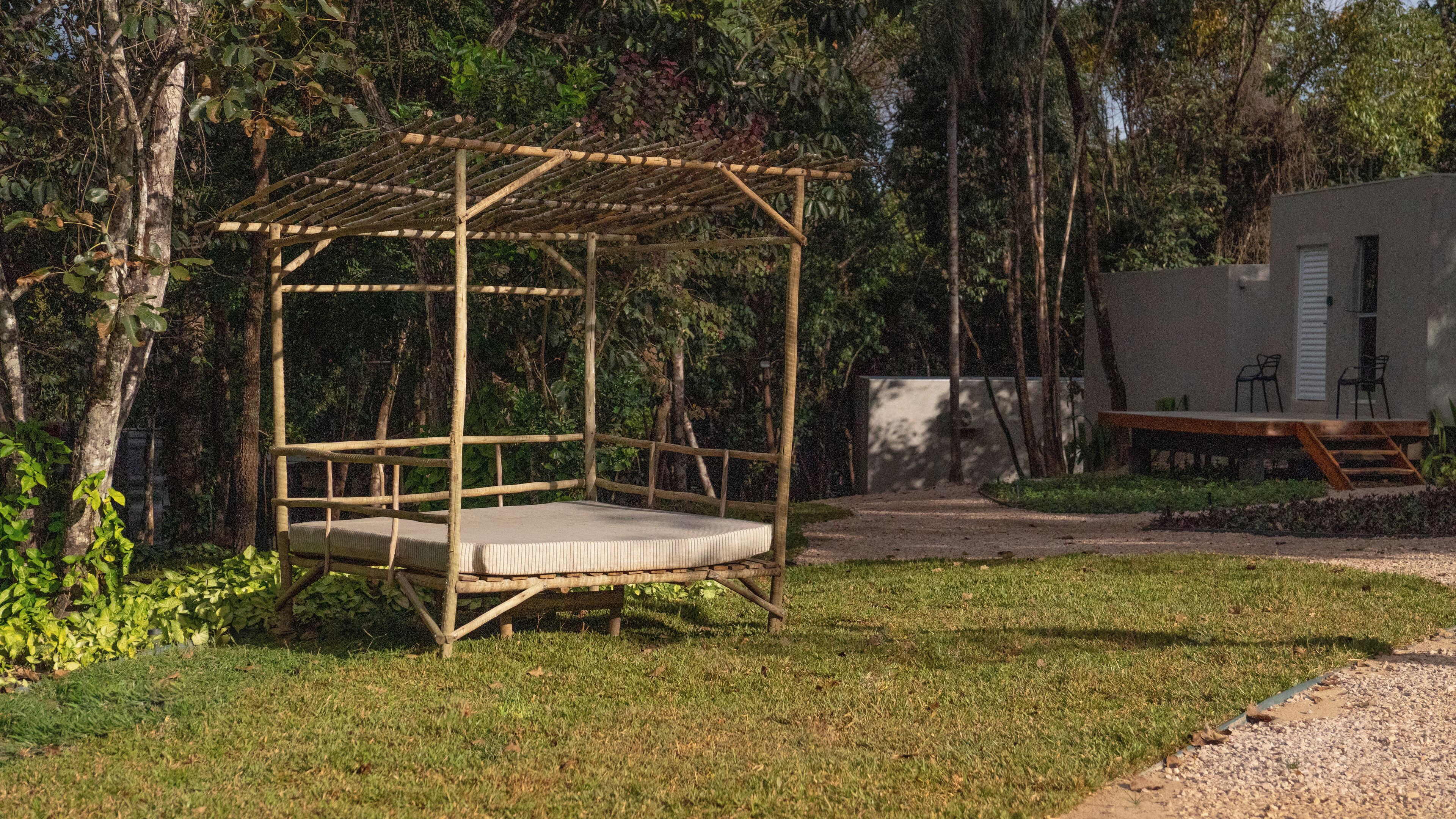 A wooden pergola with a cushioned bench in a garden setting.