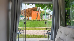 A room with a sliding glass door leading to an outdoor area with a grassy lawn, a wooden pergola, and a small orange structure. - Vila Ecco Cubo (Alto Paraiso de Goias)