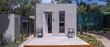 Ein modernes Haus mit Betonfassade, zwei offenen Türen und einer kleinen Terrasse mit zwei Stühlen.